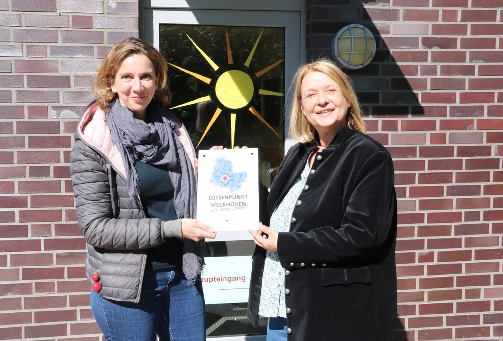 Gudrun Jüttner vom Sozialamt (l.) überreicht Birigt Adams, Leiterin des neuen Lotsenpunktes, das offizielle Schild.