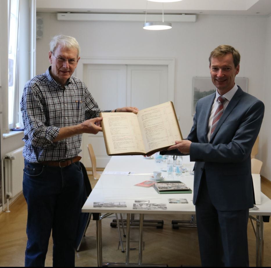 Dr. Albert Wunsch übergibt Archivleiter Dr. Jens Metzdorf ein Anlagenbuch von Bauer & Schaurte.
