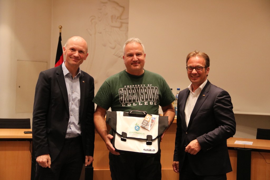 Bürgermeister Reiner Breuer (r.) und Dr. Matthias Welpmann, Umwelt-, Klima- und Sportdezernent, übergeben die Fahrradtasche an Volker Nickel.