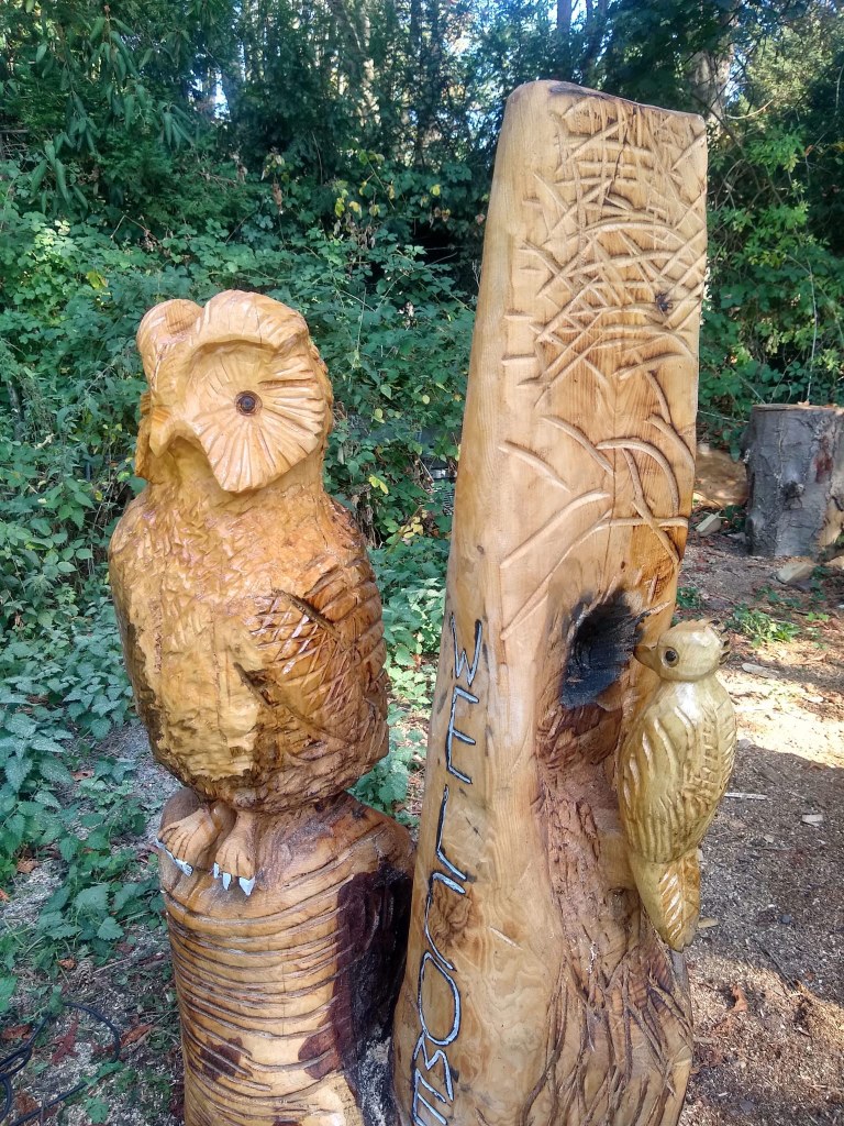 Zwei Beispiele für Carving-Kunst stehen im Park: der eine Baumstamm wurde in Form einer Eule gebracht, der andere hat die Form eines Spechts, welcher ein Loch in den Baumstamm hämmert.