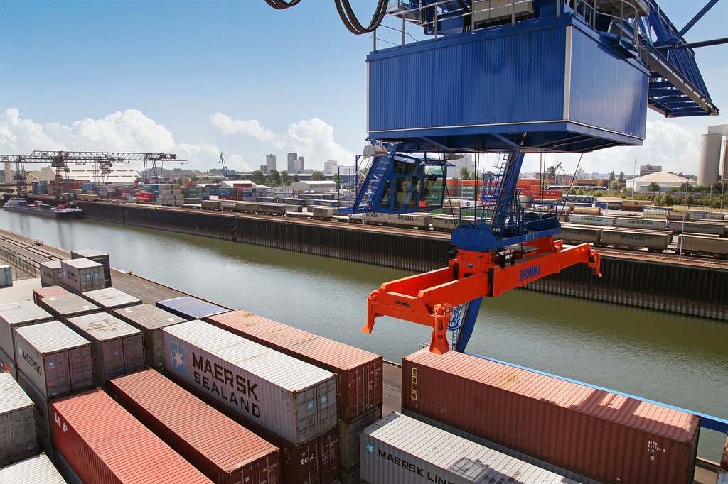 Ein Hafenkran bewegt sich über eine Reihe von Containern am Rand des Hafenbeckens.